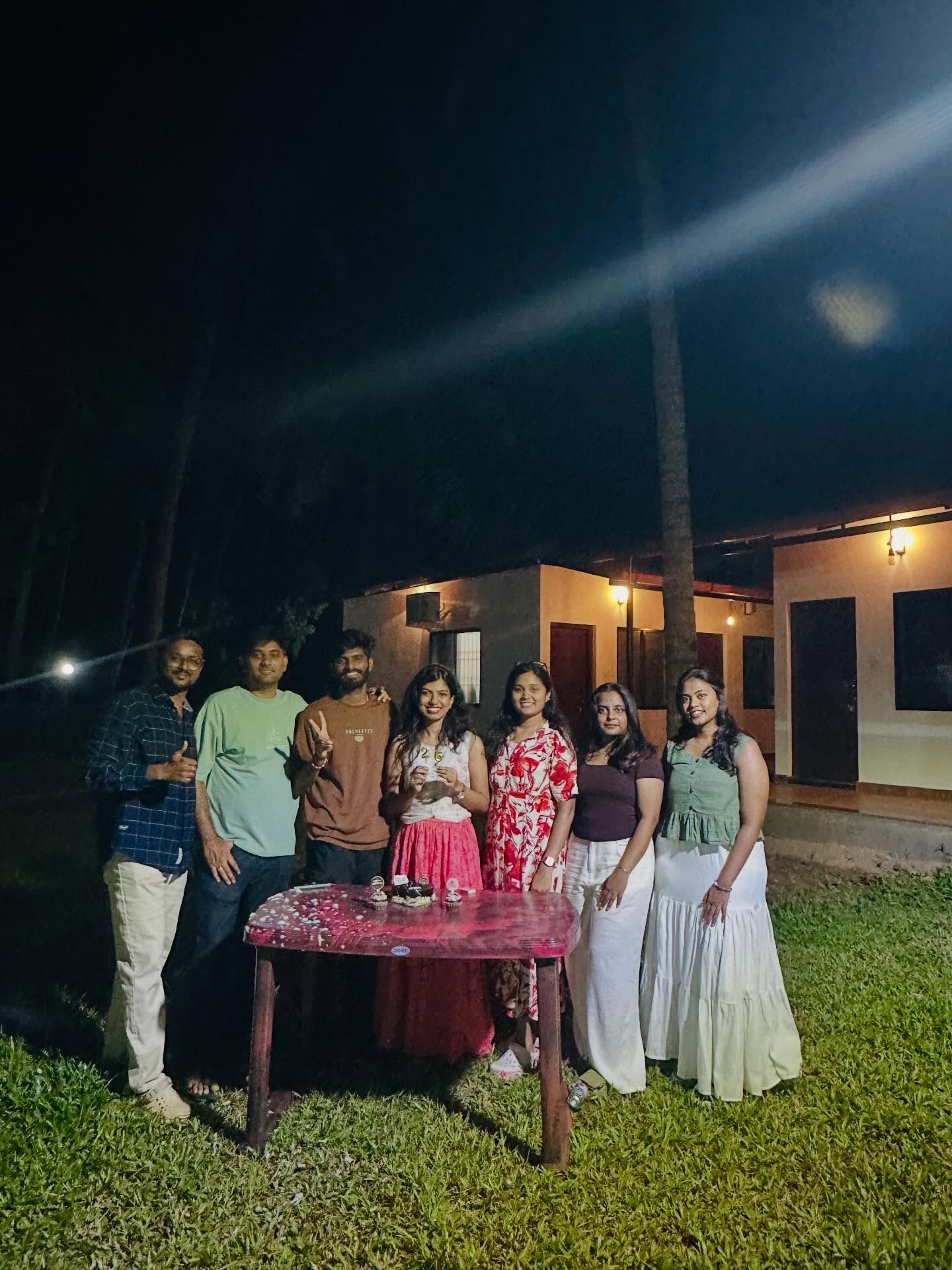 Guests celebrating an evening birthday party on the lawn outside Konkan Kuteera cottages